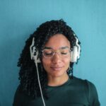 portrait photo of smiling woman in black top and glasses wearing white headphones