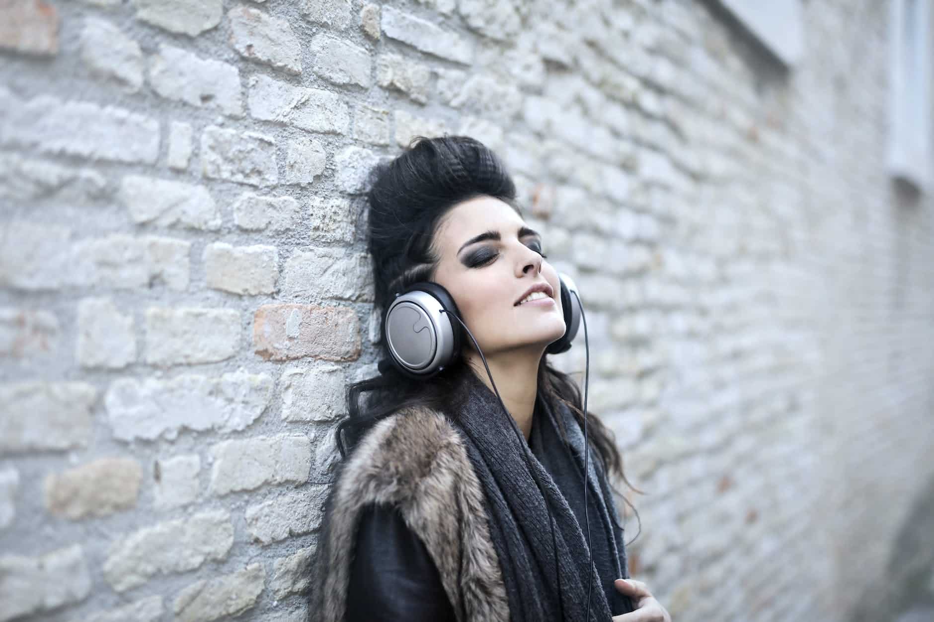 informal young woman listening to music near grunge wall