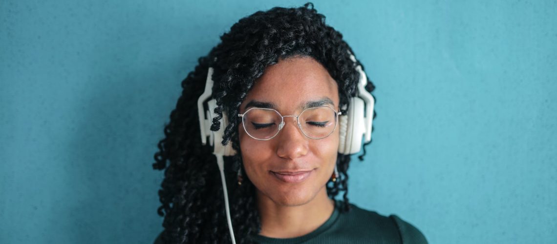 portrait photo of smiling woman in black top and glasses wearing white headphones